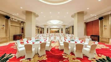 Une salle de banquet avec des tables rondes, des chaises blanches et un tapis rouge.