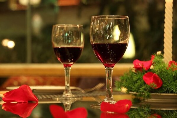 Two wine glasses on a reflective surface with red rose petals and greenery in the background. - USUM International Hotel (Chongqing)