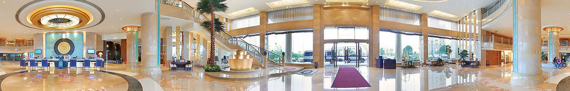 A spacious lobby with a central staircase, a reception desk, and a large window offering a view of the outside.
