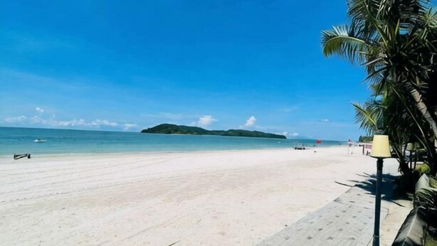 Uma praia com céu claro, areal arenoso e uma ilha ao longe.