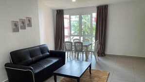 Quarto com sofá de couro preto, mesa de centro de madeira, mesa de jantar e cadeiras, e vista através de grandes janelas.