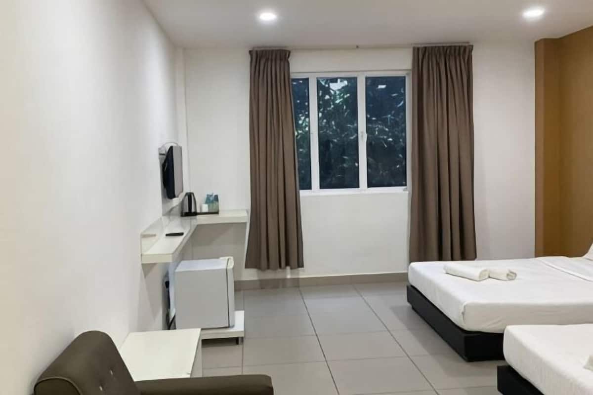 Habitación de hotel con cama, escritorio, silla, televisor y ventana con cortinas.
