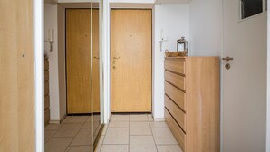 Un couloir avec des portes en bois, un sol carrelé et un petit panier posé sur un meuble.