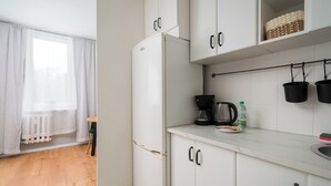 Une cuisine compacte avec des meubles blancs, un réfrigérateur encastré et un plan de travail sur lequel se trouvent une machine à café et des paniers.