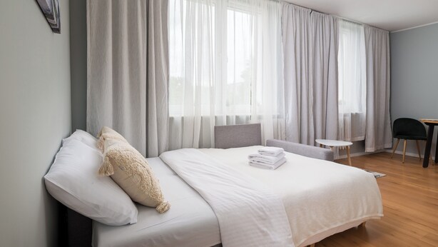 Un lit bien fait, avec du linge de lit blanc, une petite table de chevet et une chaise.
