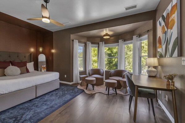 A bedroom with a bed, a ceiling fan, a desk with a chair, and large windows with curtains.