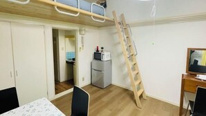 Ein Zimmer mit einem Etagenbett, einem Schreibtisch mit Computer, einem Stuhl, einem Kühlschrank und einer Mikrowelle.