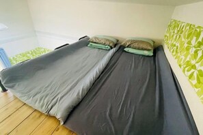 A room with two beds, each with a grey mattress and a pillow. The room has a wooden floor and a green patterned wall. - Fukuoka Hotel COCO (Fukuoka)