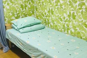 A single bed with a floral bedspread and matching pillows, a wooden nightstand, and a green leaf-patterned wall. - Fukuoka Hotel COCO (Fukuoka)