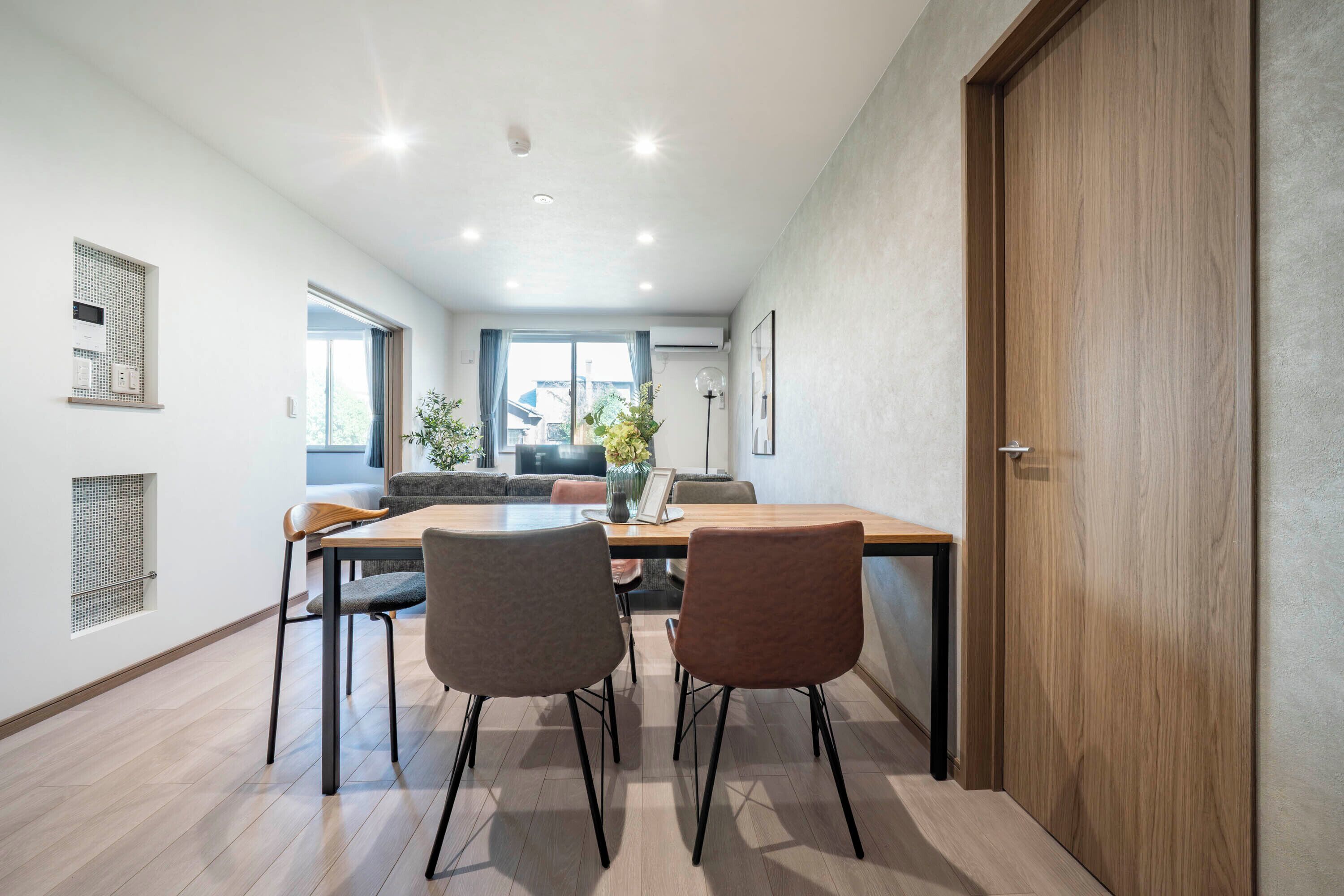 A modern dining area with a wooden table and chairs, a view of the outdoors, and a door to the right.