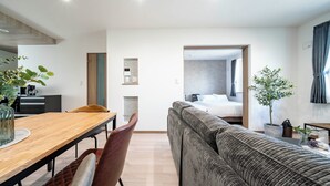 Ein modernes Hotelzimmer mit einem Holztisch, einem braunen Ledersessel, einem grauen Sofa und einem Bett mit grauer Kopfteil.