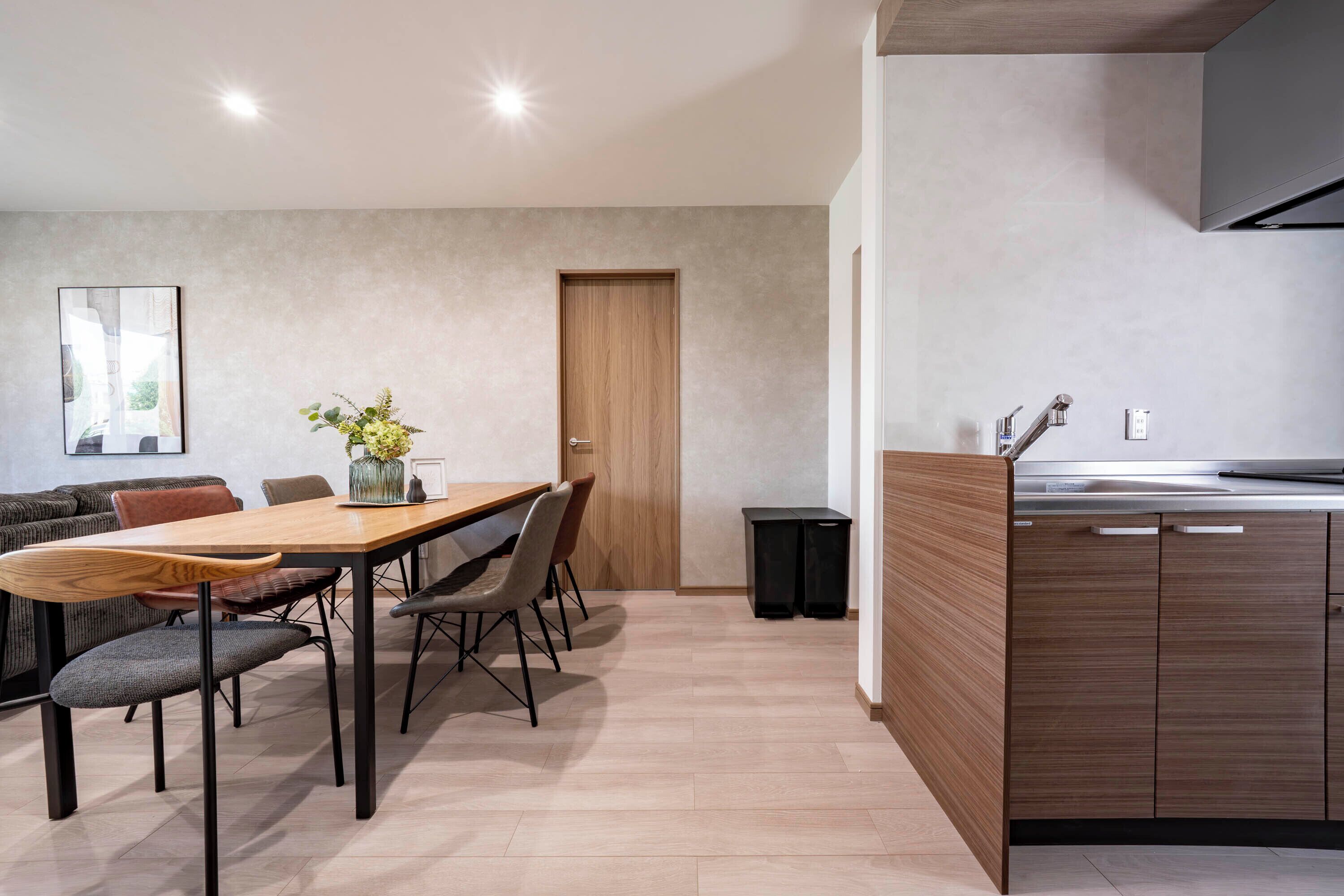 A modern kitchen with wooden cabinets, a dining area with a table and chairs, and a built-in oven.
