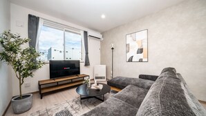 Ein modernes Wohnzimmer mit einer Couch, einem Couchtisch, einem Fernseher und einer Topfpflanze.