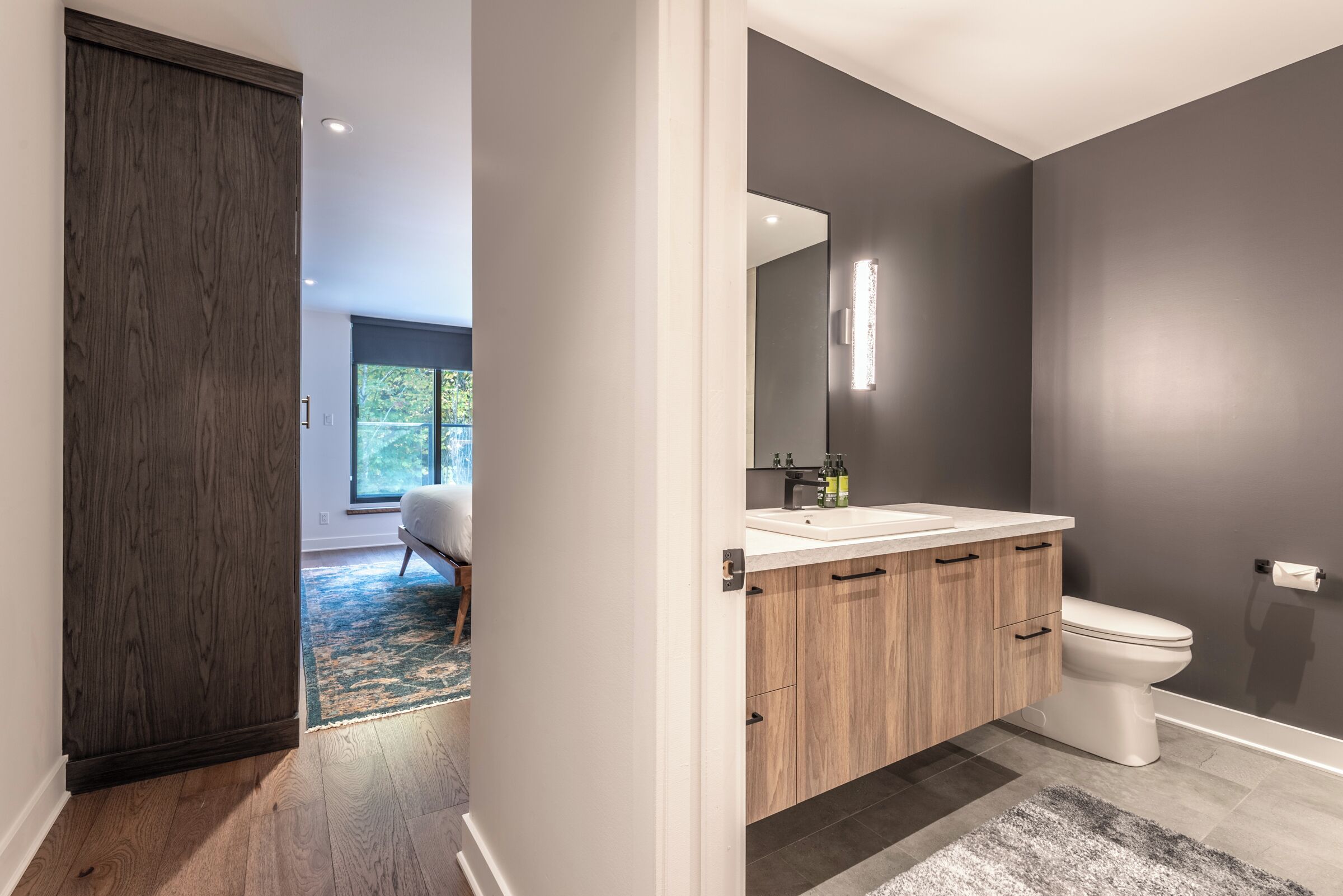 A modern bathroom with dark walls, a white sink, and a wooden vanity.