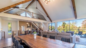 Un vaste espace dédié à la salle à manger, avec une longue table en bois, des chaises modernes et une vue sur l’extérieur grâce à de grandes fenêtres.