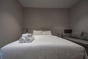 Een moderne hotelkamer met een groot bed, een bank en netjes gevouwen handdoeken op het bed.