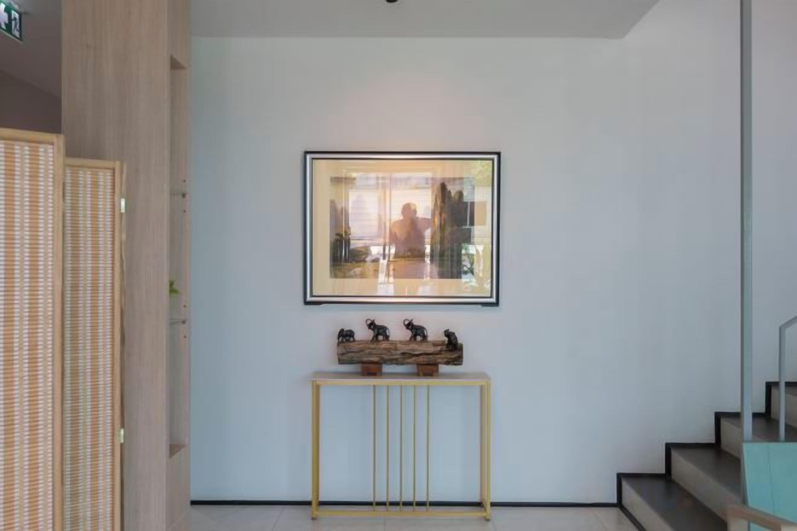 Un couloir avec un tableau encadré au mur, une petite console ornée de figurines et un escalier sur la droite.