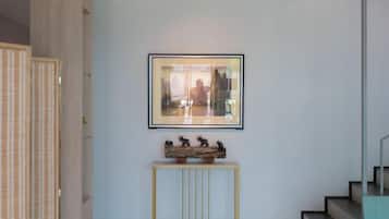 Un couloir avec un tableau encadré au mur, une petite console ornée de figurines et un escalier sur la droite.