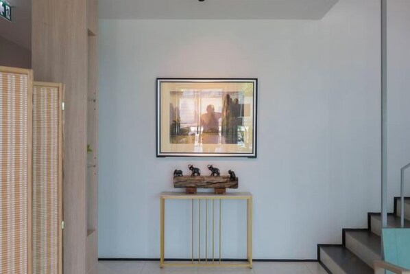 A hallway with a framed picture on the wall, a small console table with figurines, and a staircase to the right.