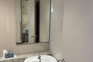 Een badkamer met een witte wastafel, een spiegel en een douchecabine van glas.