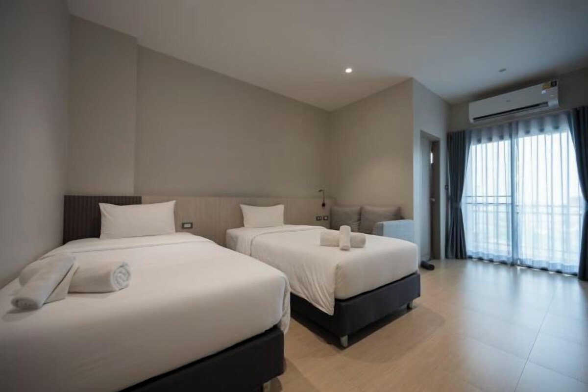 A hotel room with two beds, a large window with curtains, and an air conditioning unit.