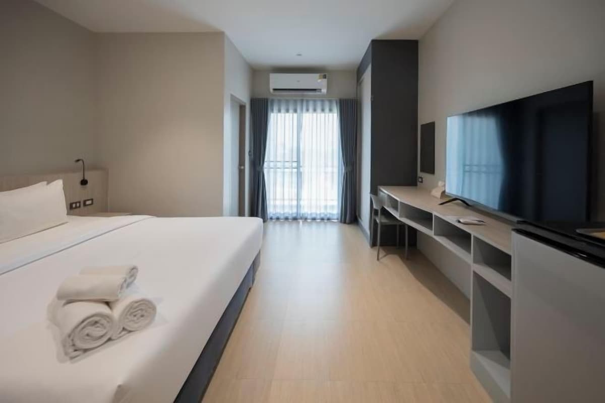 A hotel room with a bed, a TV, a desk, and a window with curtains.