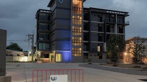 Un hotel moderno de varios pisos con una entrada destacada y un camino de acceso con portón.