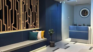 Un área de recepción moderna con una paleta de colores azul y blanco, un panel decorativo de madera, un rincón de descanso con cojines y un mostrador de recepción.