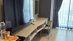 Una habitación moderna con una televisión de pantalla plana grande, un escritorio de madera, una silla y un ventanal con cortinas.