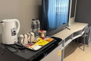 A hotel room with a kitchenette, a kettle, water bottles, a coffee maker, and a tray with food items. - Citywan Ratchaburi (Ratchaburi)