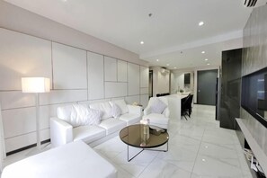 A modern living room with a white sofa, a coffee table, a TV, and a dining area. - 8 Kia Peng Suites Residence by Scape Stay (Kuala Lumpur)