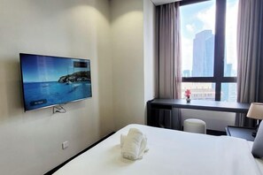 A hotel room with a bed, a desk, a TV displaying a coastal scene, and a window with curtains. - 8 Kia Peng Suites Residence by Scape Stay (Kuala Lumpur)
