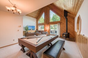 A cozy room with a pool table, a bench, a fireplace, and a large window overlooking greenery.