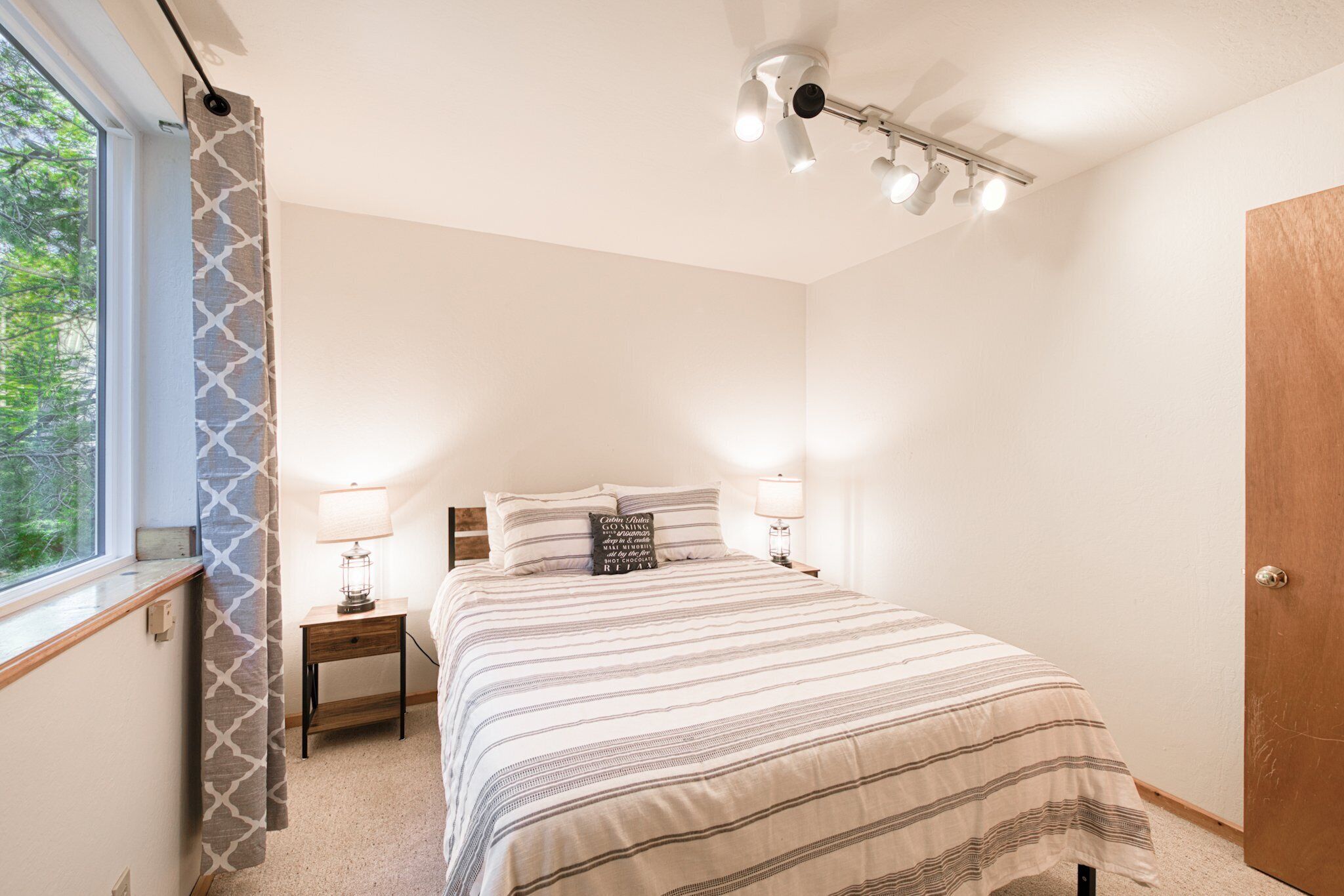 Une chambre à coucher avec un lit, des lampes de chevet, une fenêtre avec des rideaux et un ventilateur de plafond.