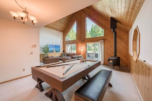 A cozy room with a pool table, a bench, a fireplace, and a large window overlooking greenery.