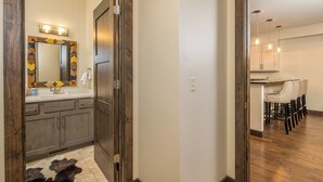 A modern bathroom with a wooden door, a mirror with a decorative frame, and a sink. - New! Hot Tub, Town Center, Western Luxe Delight! (Big Sky)