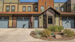 A multi-story building with a garage entrance, a small porch, and a flag. - New! Hot Tub, Town Center, Western Luxe Delight! (Big Sky)