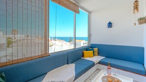 Ein Zimmer mit einem großen Fenster, einem blauen Sofa, einem kleinen Tisch mit Flasche und Gläsern sowie einem an der Wand befestigten Vogelhäuschen.