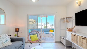 Ein modernes Wohnzimmer mit einem grauen Sofa, einem runden Sessel mit grüner Kissen und einem kleinen weißen Tisch. Ein Fernseher ist an der Wand angebracht.