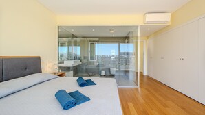 A modern bedroom with a large bed, a bathroom with a glass shower, and a city view. - Villa Aleksandra - Private Pool (Albufeira)