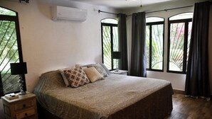 A bedroom with a large bed, a bedside table, a lamp, and a window with curtains. - Casa Suryaa Ananda in the heart of Ojochal (Provincia de Puntarenas)