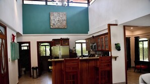 A spacious kitchen with a central island, wooden cabinets, and a large window. - Casa Suryaa Ananda in the heart of Ojochal (Provincia de Puntarenas)