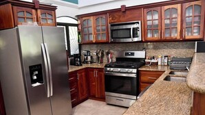 A kitchen with a stainless steel refrigerator, a microwave, an oven, granite countertops, wooden cabinets, and a coffee maker. - Casa Suryaa Ananda in the heart of Ojochal (Provincia de Puntarenas)
