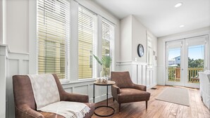 A room with two brown leather chairs, a small round table with a plant, and a large window with blinds. - Seagrove Beach Retreat | Steps to the Sand (Seagrove Beach)