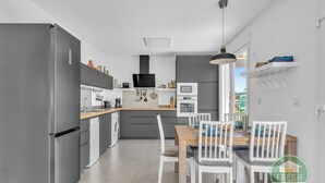 A modern kitchen with grey appliances, a wooden dining table, and white chairs. - Family cottage in Benajarafe w pool and sea view (Vélez-Málaga)