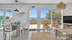 A modern dining area with white chairs, a wooden table, and a large window offering a view of the sea. - Family cottage in Benajarafe w pool and sea view (Vélez-Málaga)