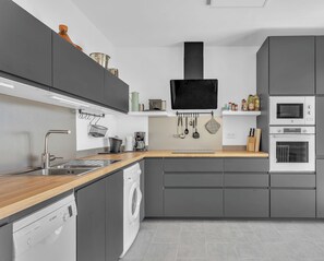 Een moderne keuken met grijze kastjes, een houten aanrecht, een Bosch vaatwasser, een inbouwoven en een magnetron.