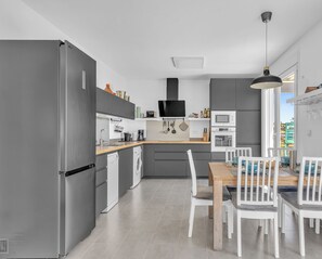 A modern kitchen with grey appliances, a wooden dining table, and white chairs. - Family cottage in Benajarafe w pool and sea view (Vélez-Málaga)