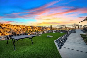 Une terrasse avec un mur en pierre, une table en métal et une zone herbeuse.