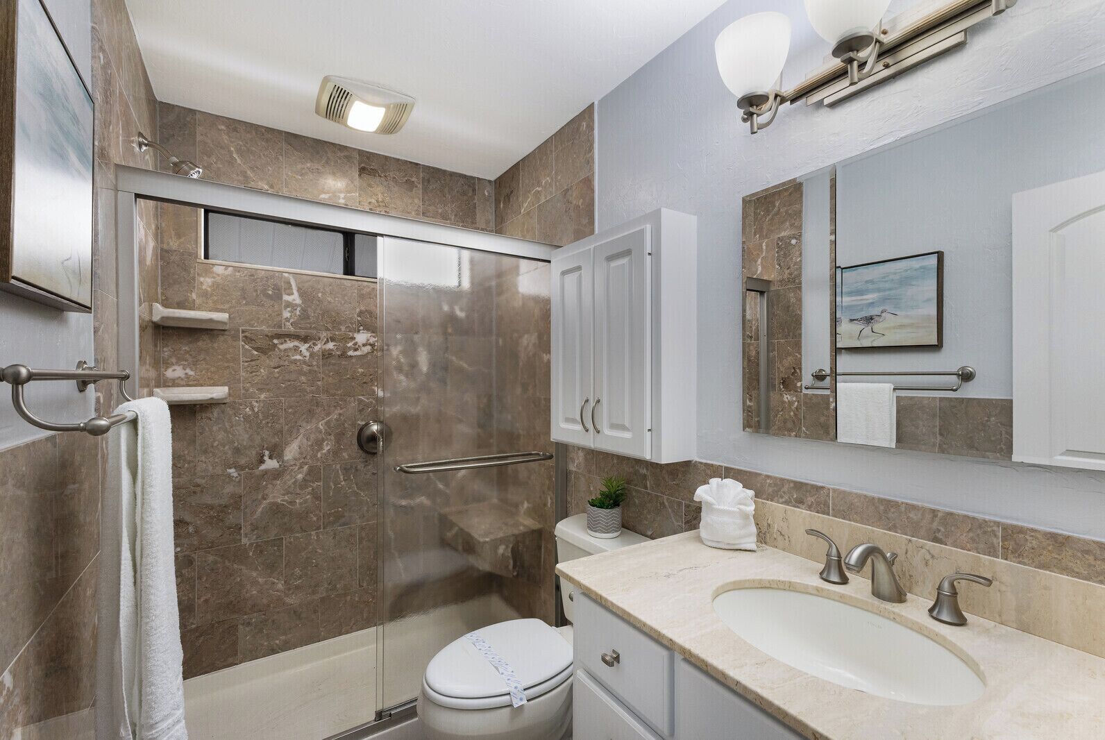 A modern bathroom with a glass shower enclosure, a toilet, a sink with a vanity, and a large mirror.